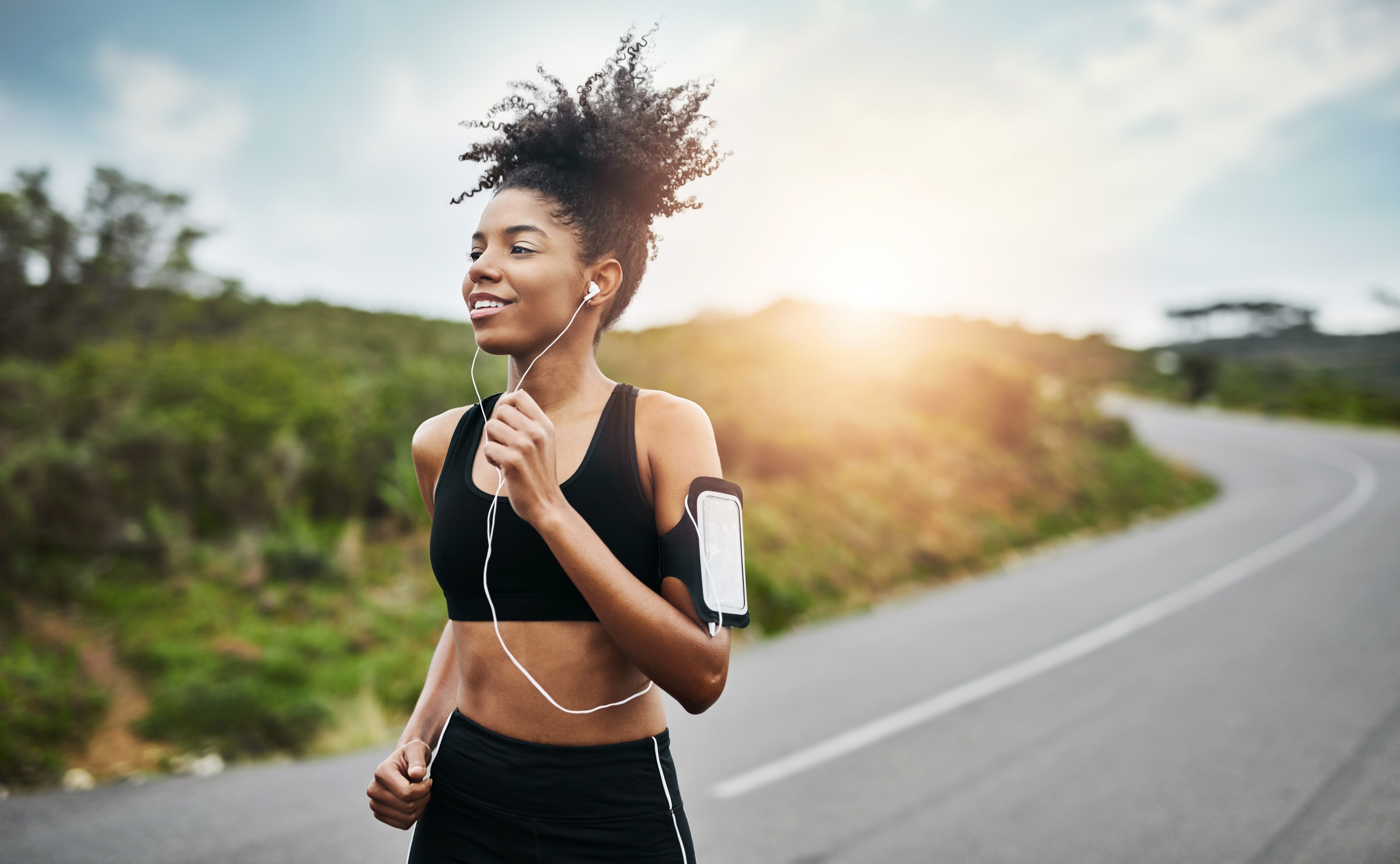 A woman listens to her headphones while she jogs down a country road.
