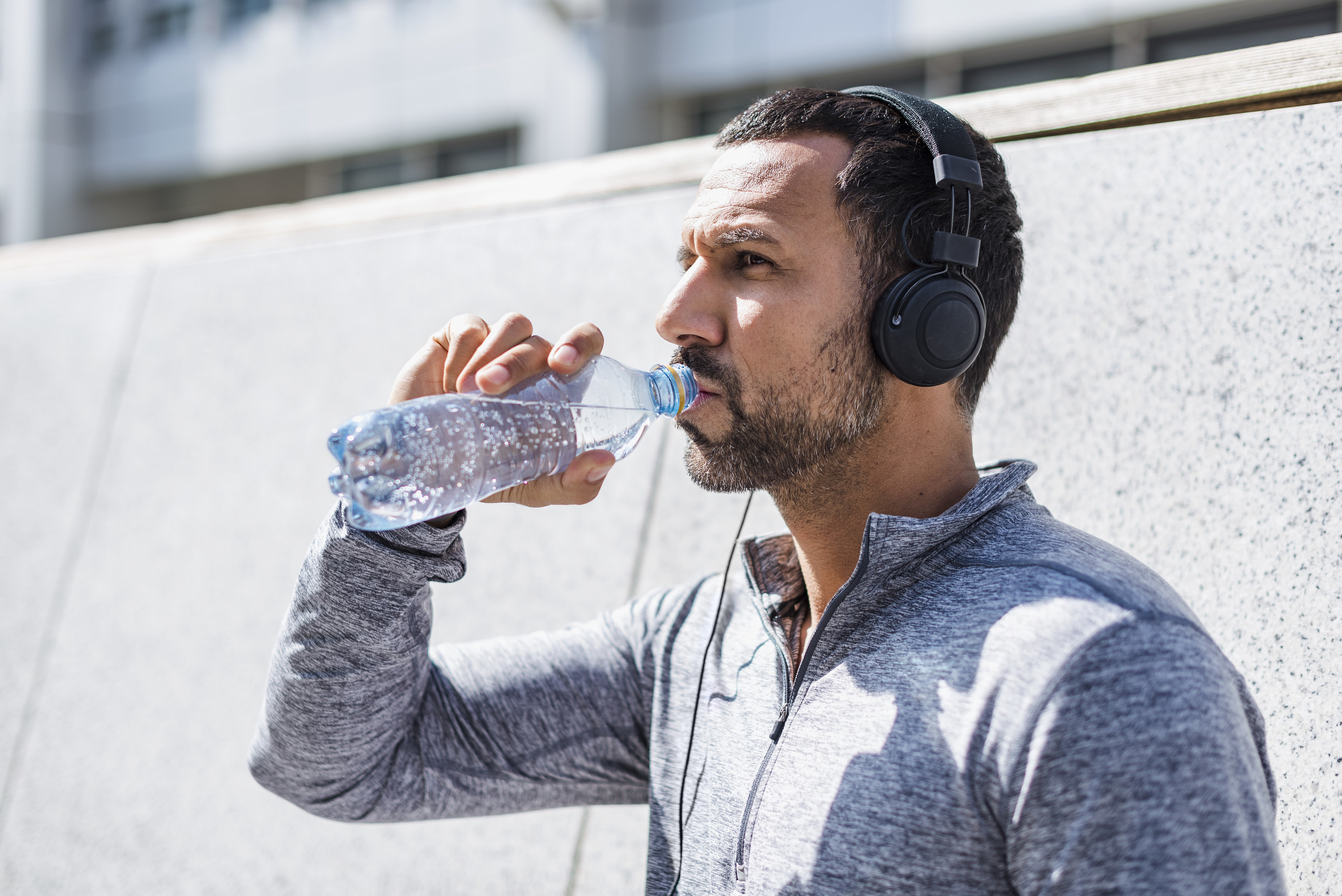 A man wearing headphones drinks from a water bottle