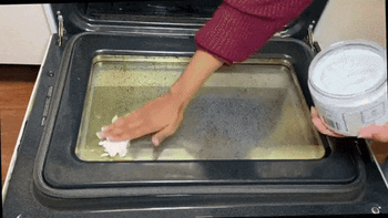 gif of someone rubbing the paste on a dirty oven door and wiping the door clean with a cloth