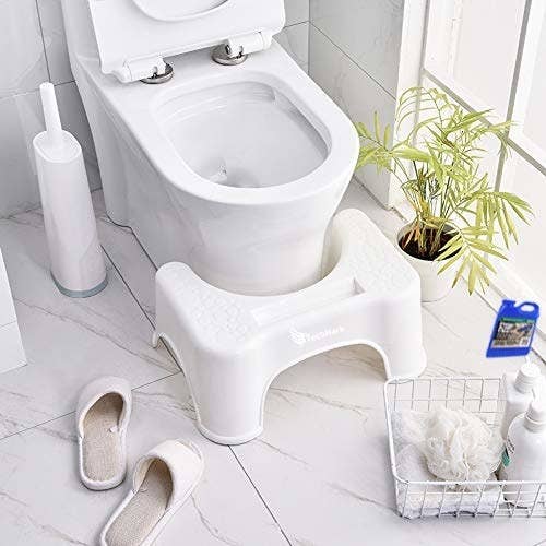 A squat step stool kept in front of toilet seat in bathroom
