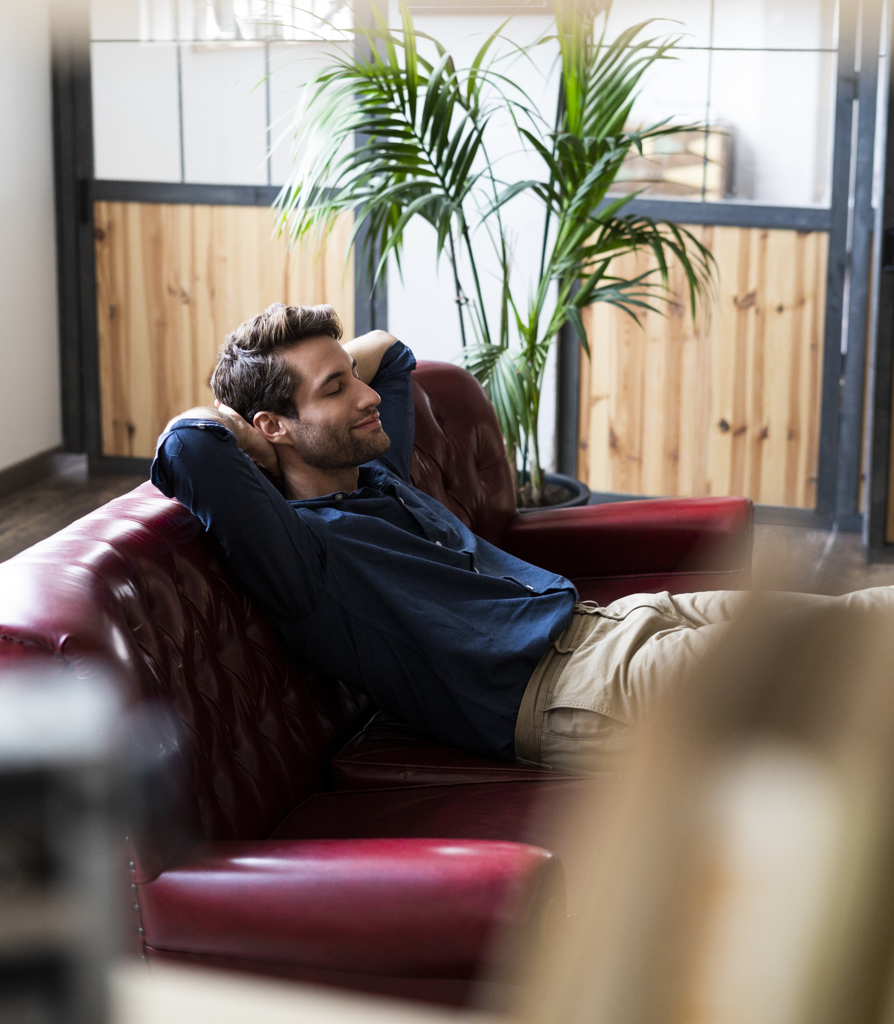 A guy on a couch with legs propped up and eyes closed, plants and office doors around him