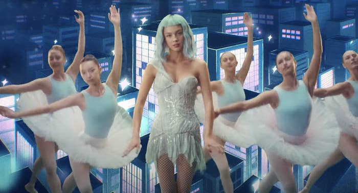 Olivia wears an sparkly one-shouldered short dress with fishnet stocking and a wig with bangs