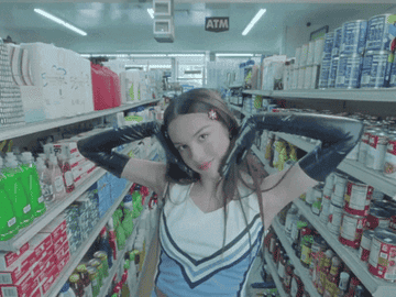 Olivia in the middle of a grocery store aisle wearing a cheerleading outfit and long gloves
