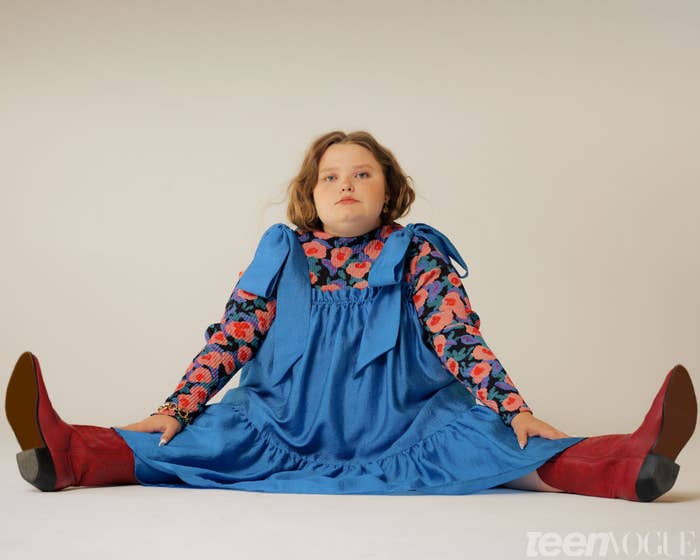Alana sitting on the floor in a dress, floral print shirt, and boots