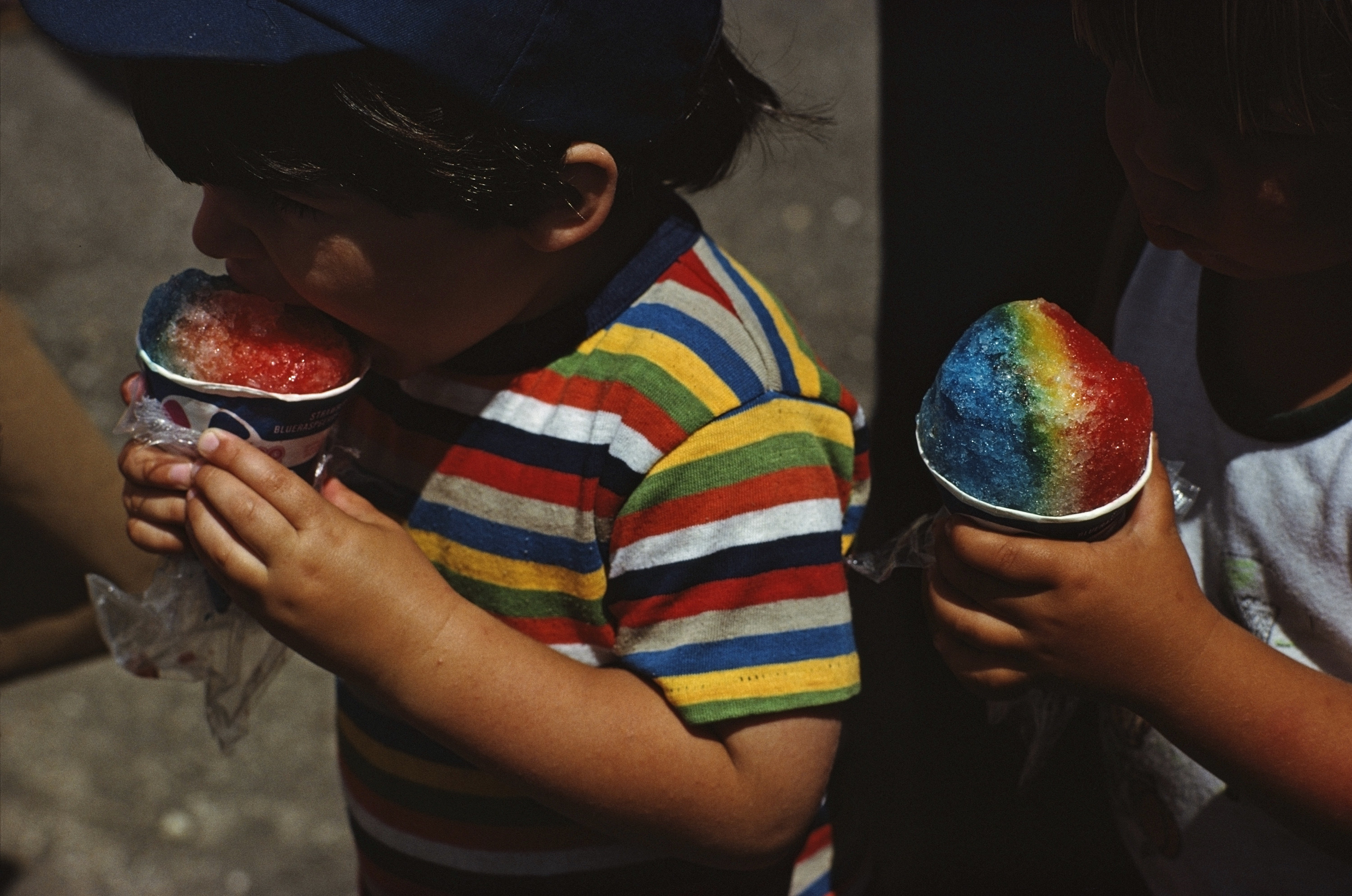 Two children hold rainbow colored snow cones at the county fair in Maine