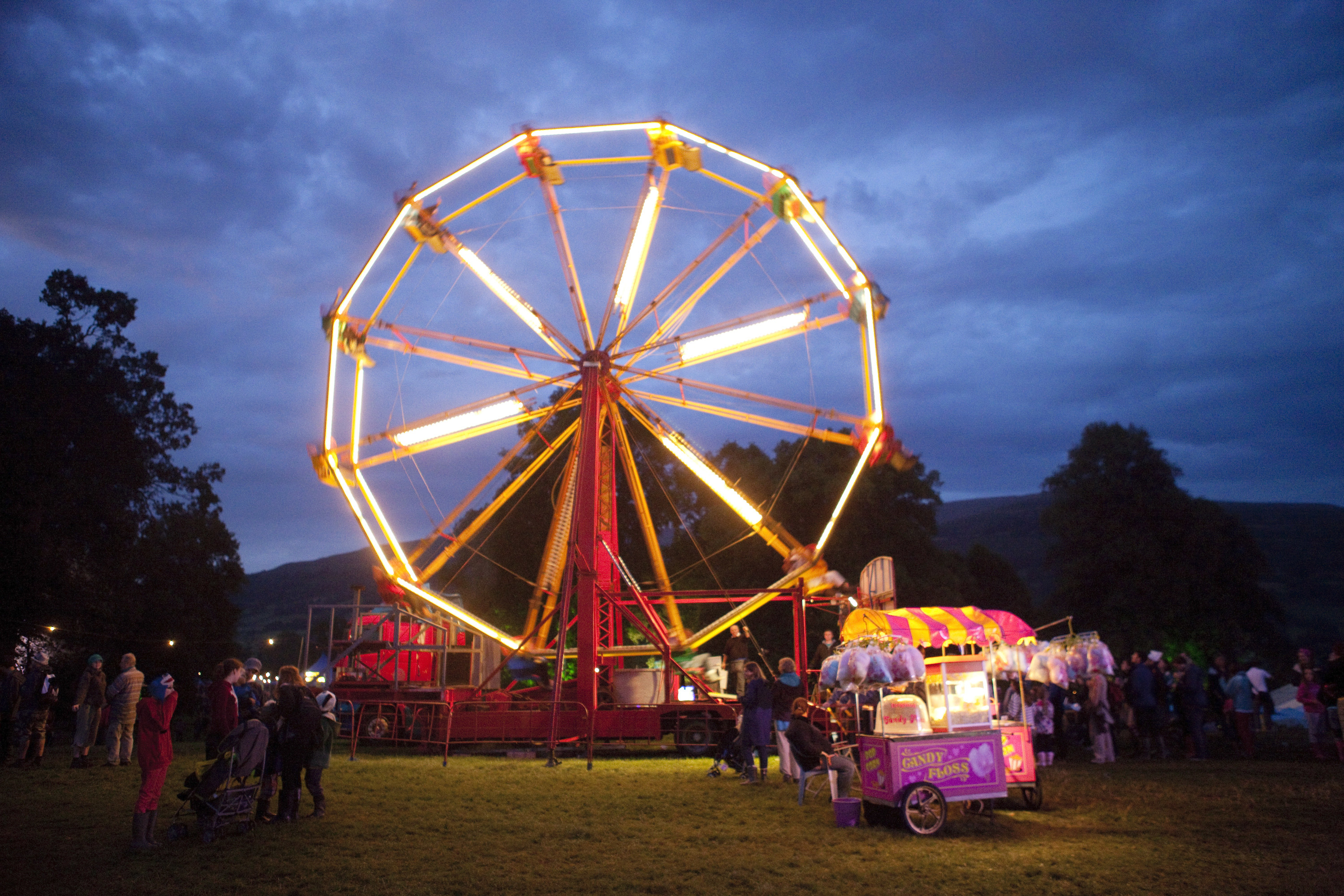 A ferris wheel and cotton candy stand light up the evening sky at the Green Man Festival