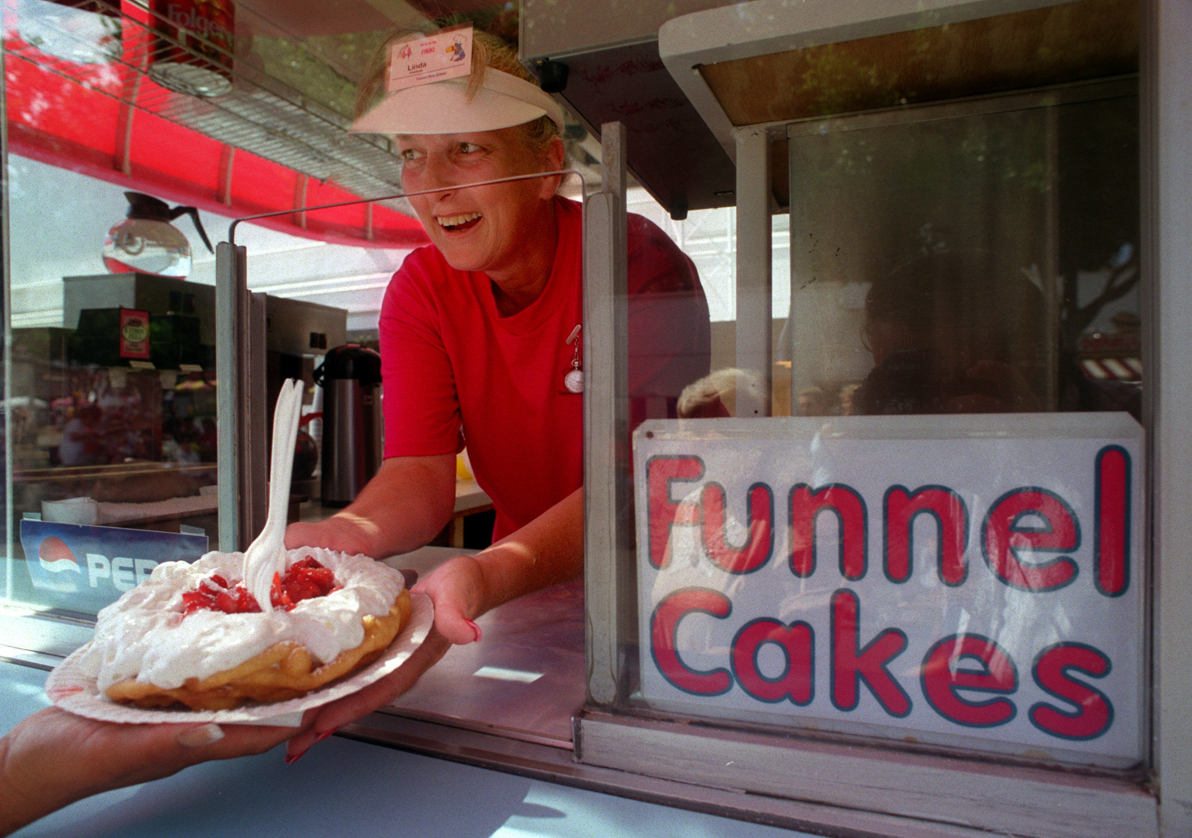 A female worker at a funnel cake stand passes a guest a cake