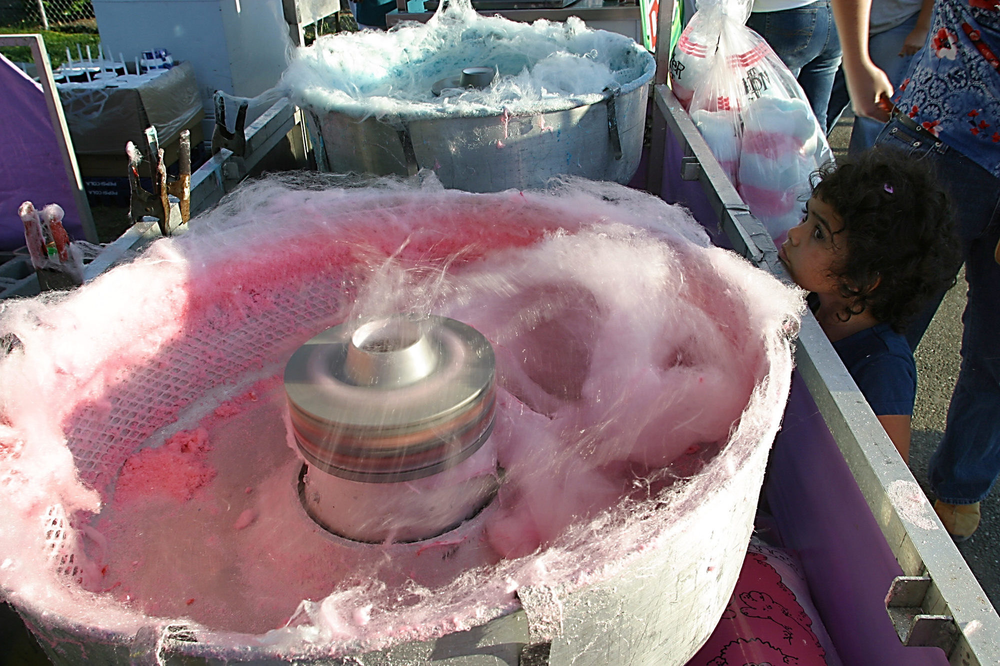 A child looks up at two barrels that spin pink and blue cotton candy