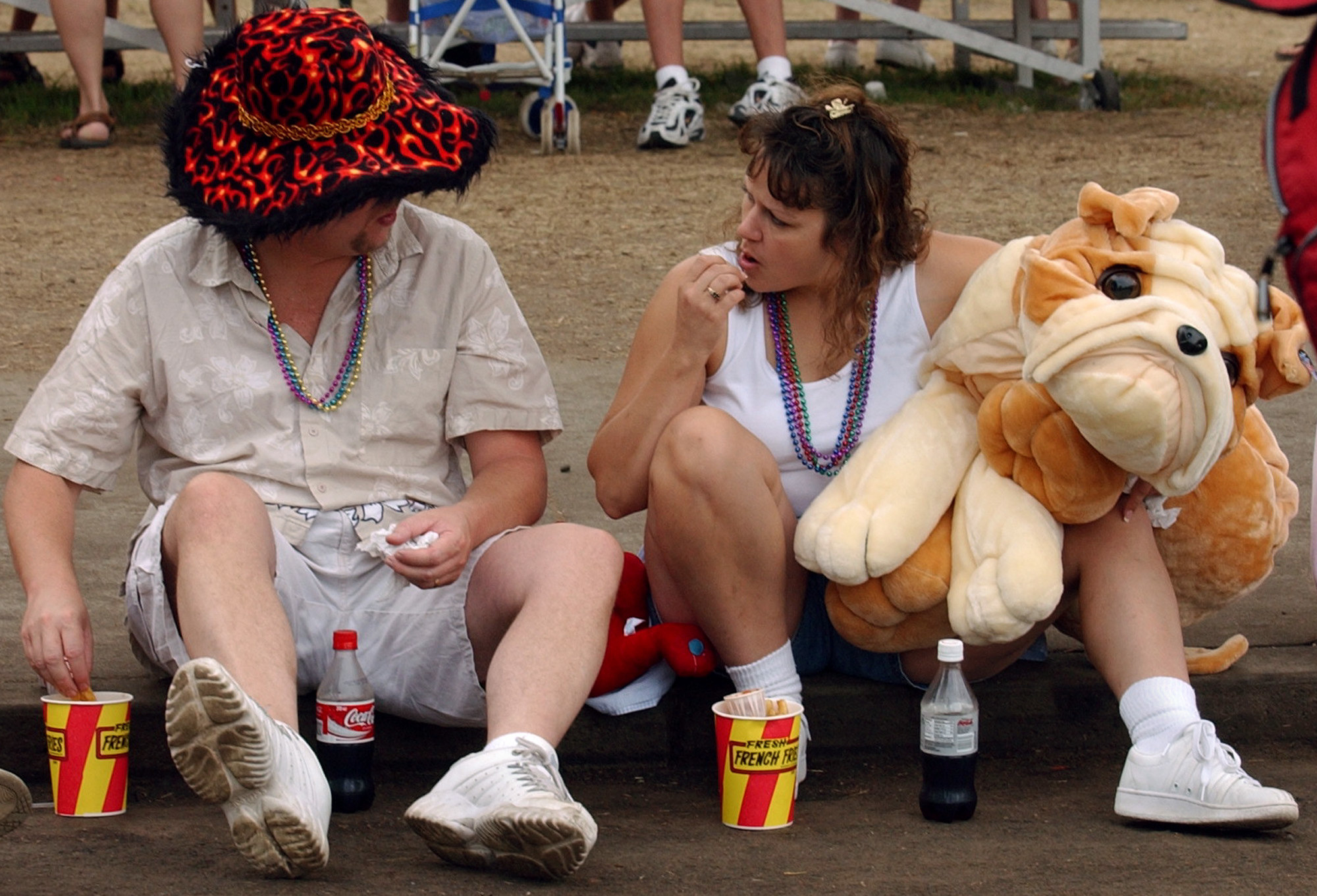 Two people eat popcorn and sit on a curb with prizes from the Minnesota State Fair