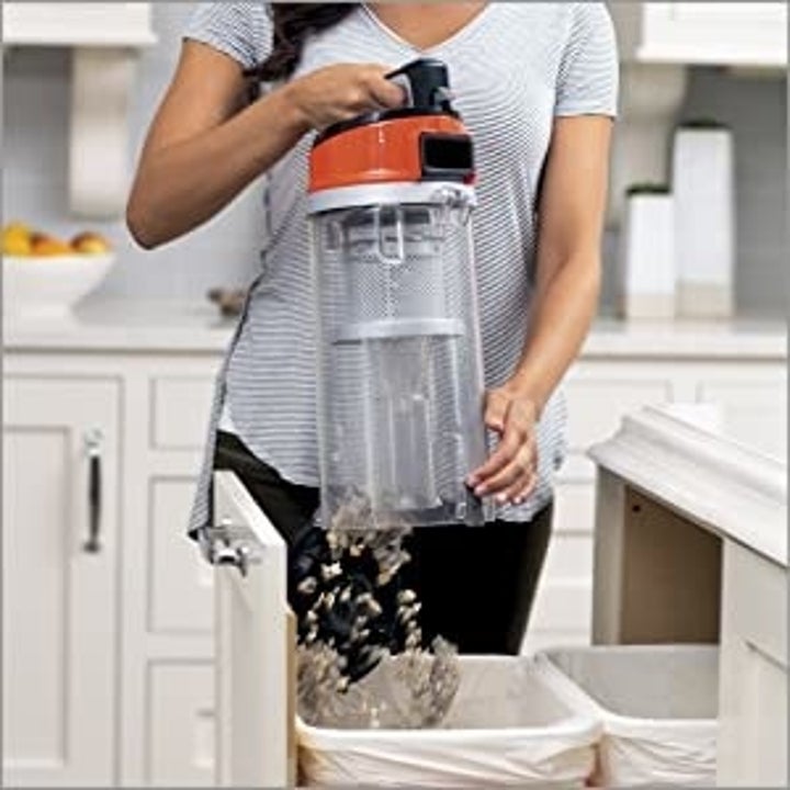 model emptying dirt container by holding it over trash can and pressing a button