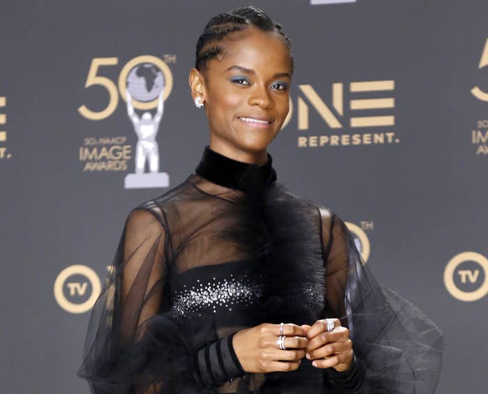 Letitia smiles while wearing a sheer long sleeve black dress with a sequined bandeau top underneath