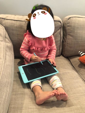 Reviewer's child using the stylus on the blue writing tablet