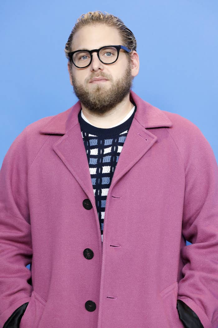 Jonah Hill poses on the red carpet while wearing glasses and a coat and sweater