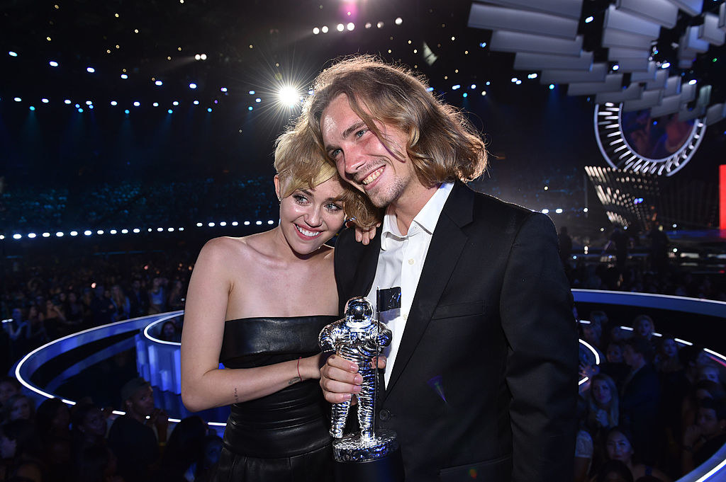 Miley Cyrus posing with a man holding her Moon Man award at the 2014 MTV VMAs