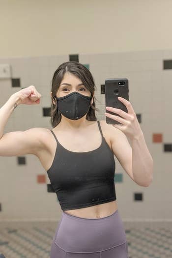 reviewer wearing the top in black and flexing while taking a selfie