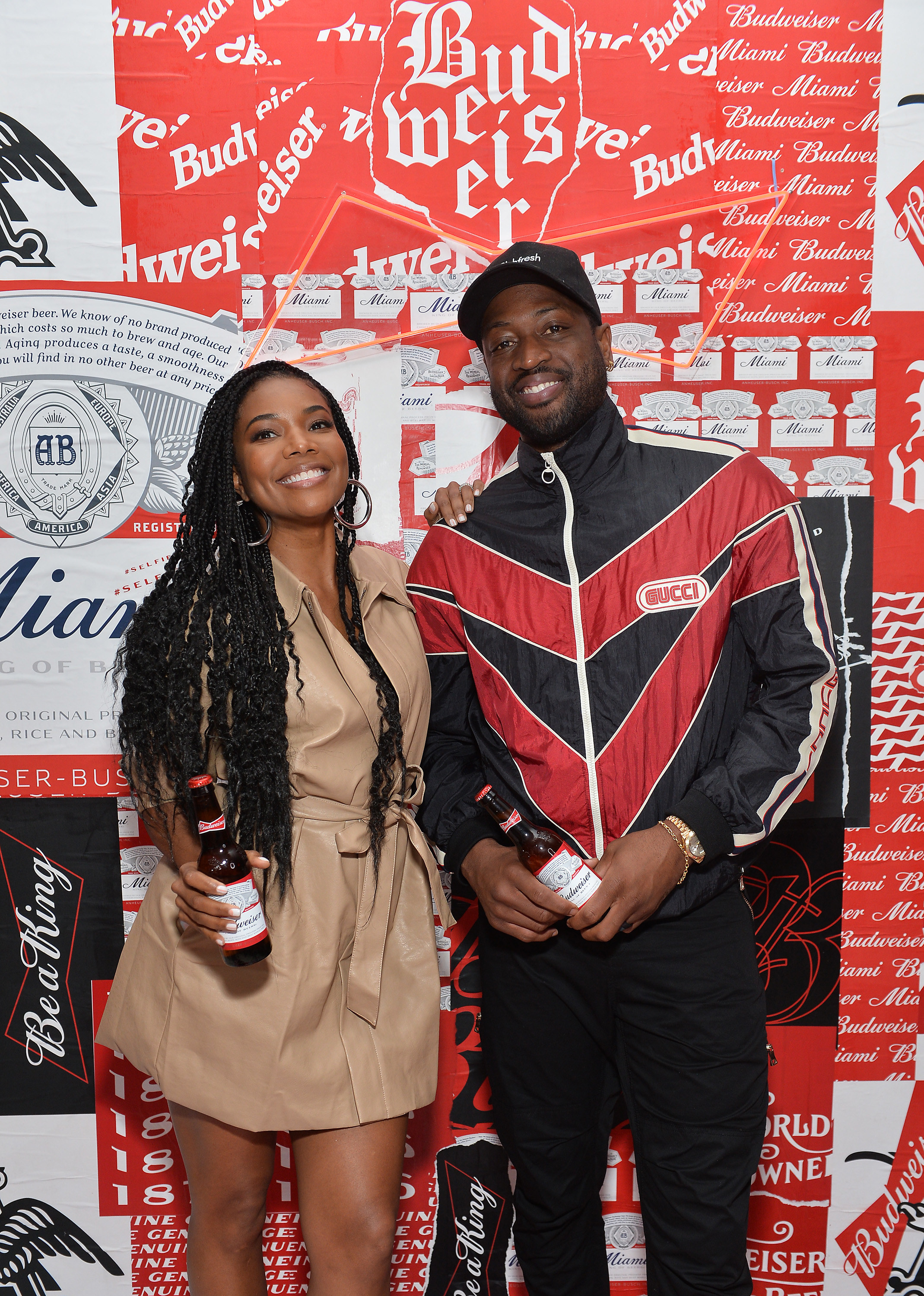 Gabrielle and Dwayne smiling for a photo as they both hold bottle of Bud Light beer at an event