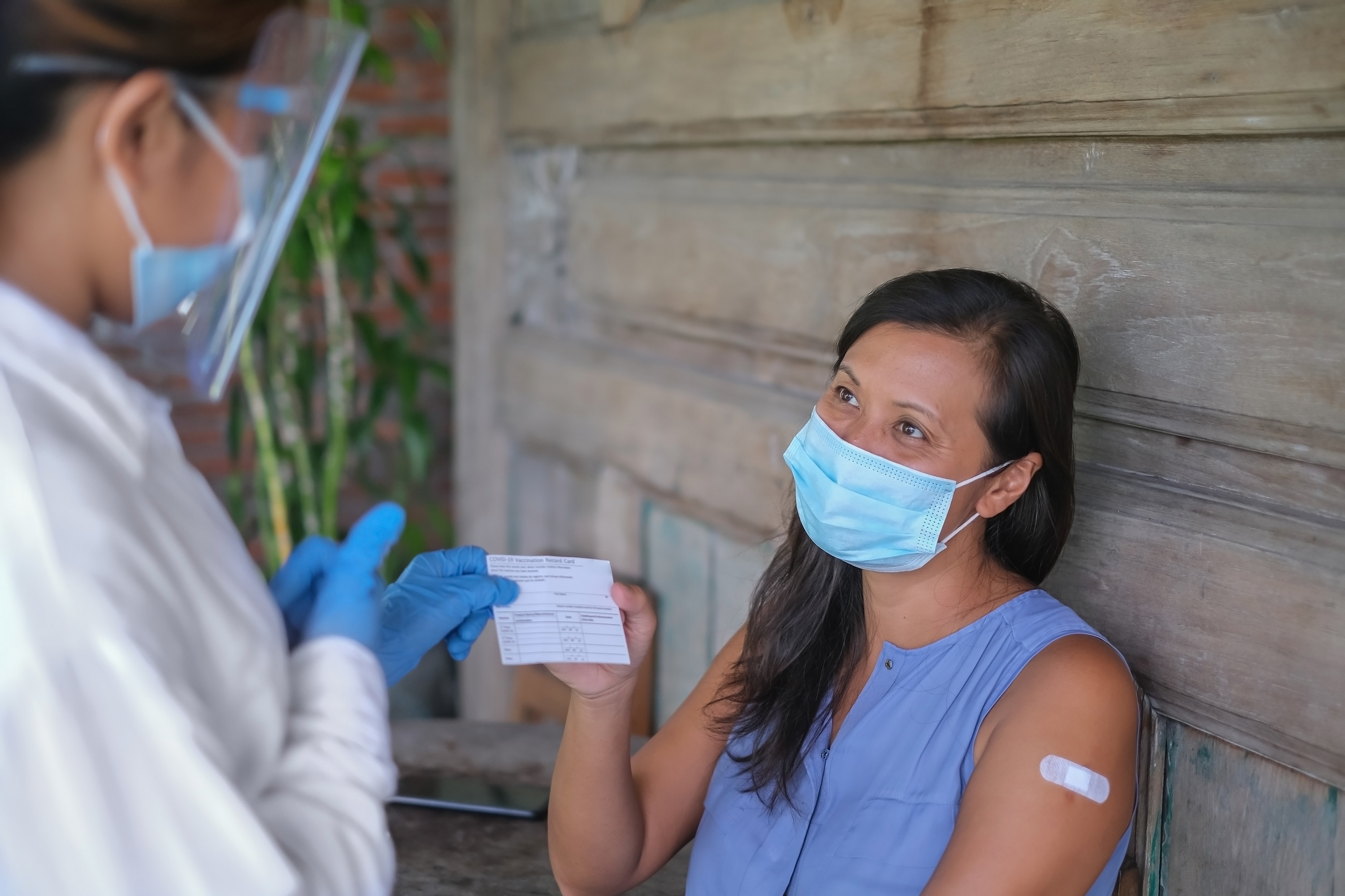 Woman with protective face mask receiving a COVID-19 vaccination record card from a healthcare worker