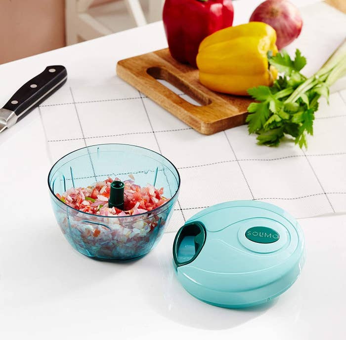 Manual food chopper with chopped onions and tomatoes in it