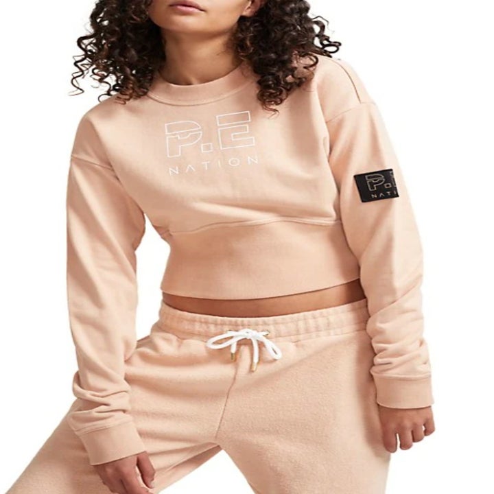 model wearing the sweatshirt in tan with "P.E Nation" on the front and matching sweatpants