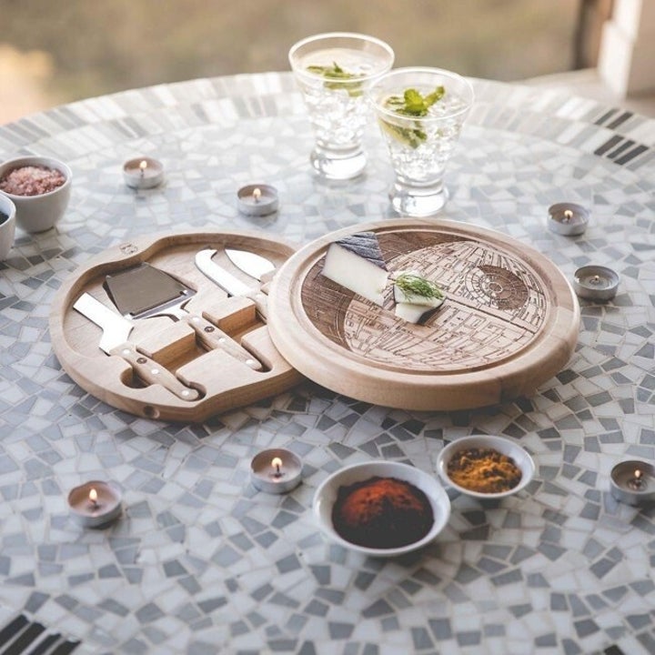 round two-piece cheeseboard in the shape of the death star from star wars. it has four cheese serving and cutting utensils packed inside one half.