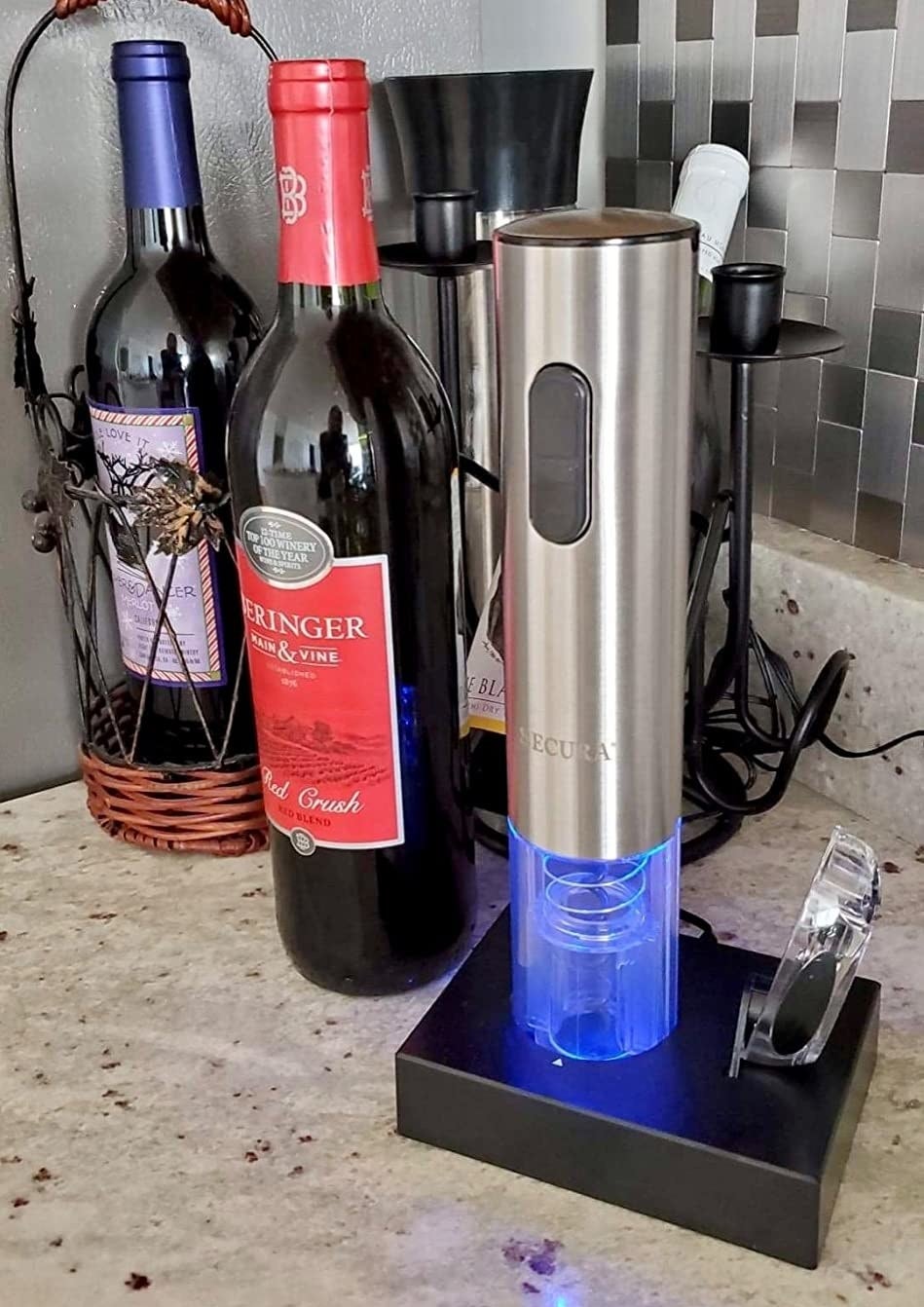 a reviewer photo of the electric corkscrew sitting on its charging dock next to the included foil cutter 