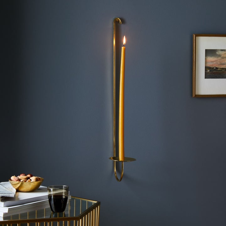 long, thin curved candle holder mounted on the wall with a very tall single candle lit inside of it