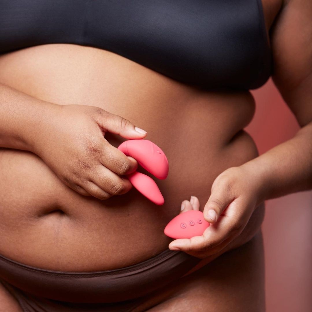 Model holding pink vibrator and pink wireless remote in front of torso