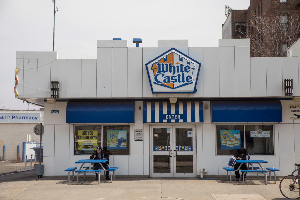 The outside of a White Castle restaurant with two people sitting at the tables in front