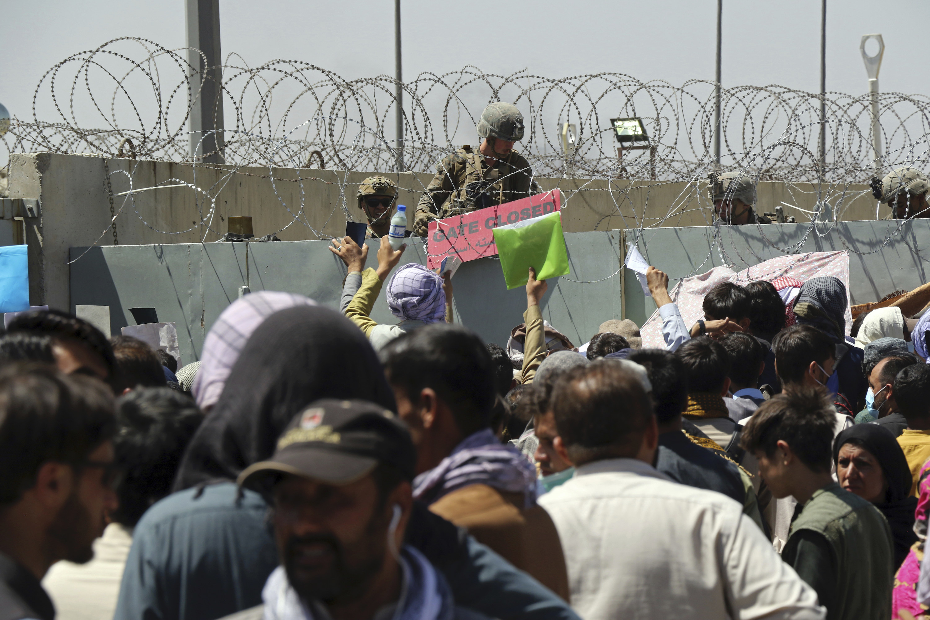 A large crowd gathers outside a gate at the airport in Kabul as a guard posts a sign that reads &quot;Gate Closed&quot;