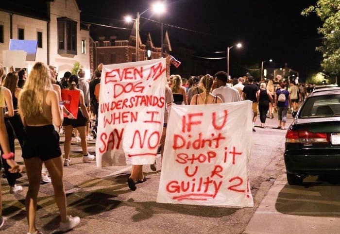 People crowded in the street carry spray-painted signs that read "even my dog understands when I say no" and "if you didn't stop it, you are guilty too"