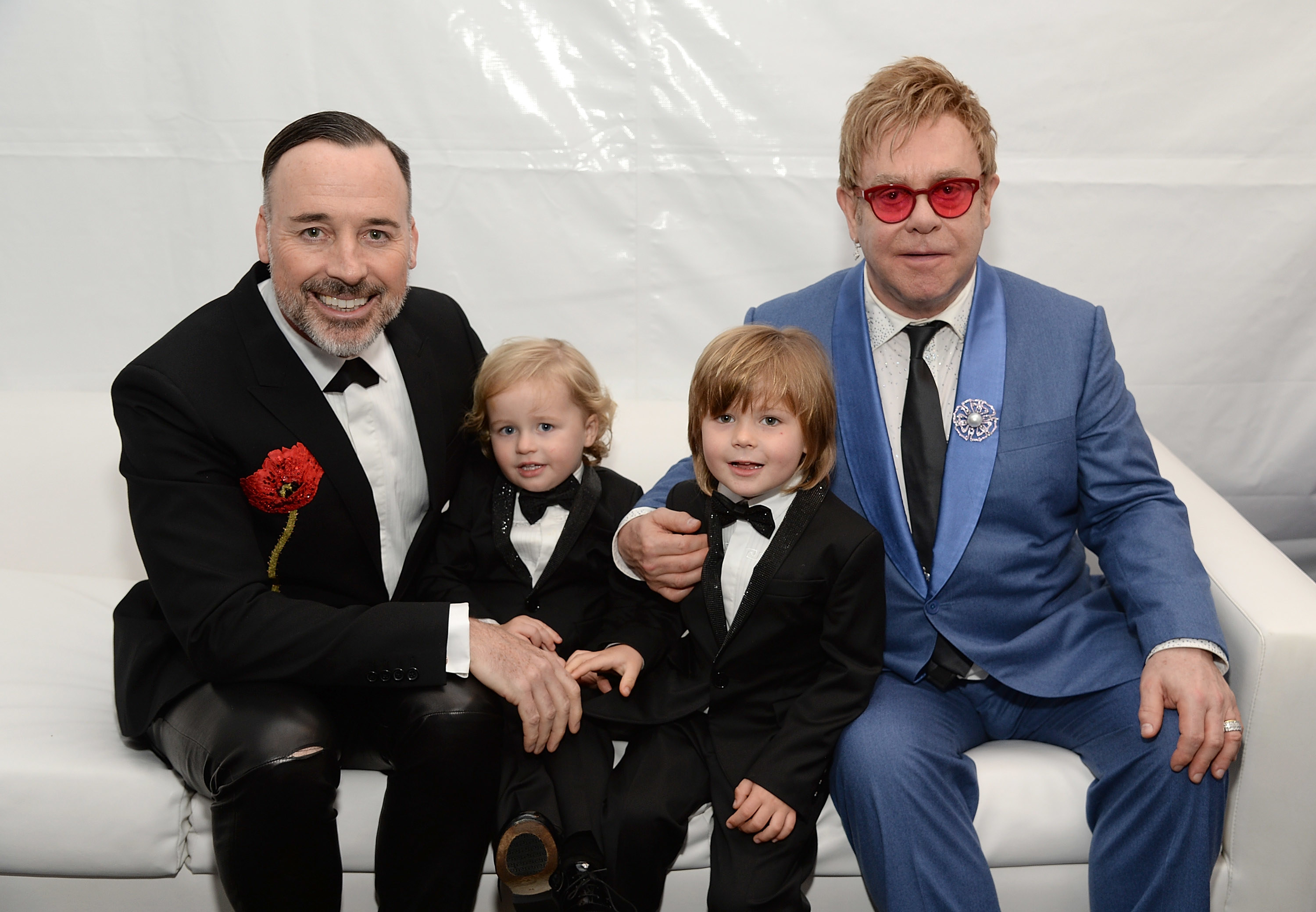 David and Elton sit on a couch and put their arms around their young twin sons