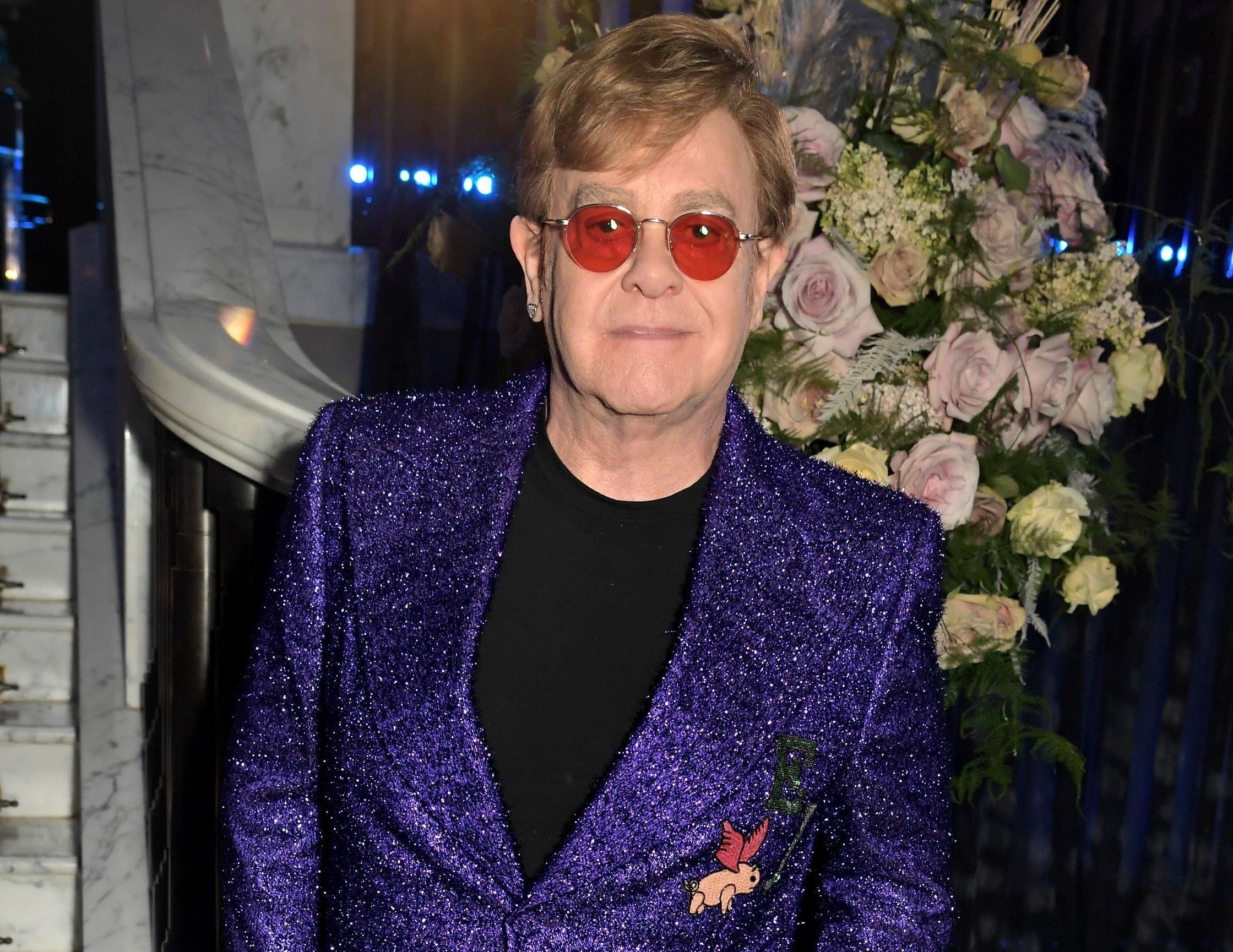 Elton wears a purple sparkly blazer and red tinted glasses
