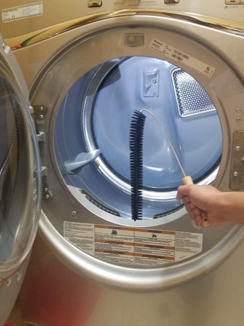 person using long brush to clean out the lint trap in a front-load clothes dryer