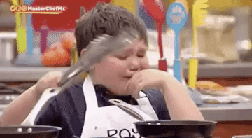 Kid crying while flipping a beef patty in a pan with tongs.