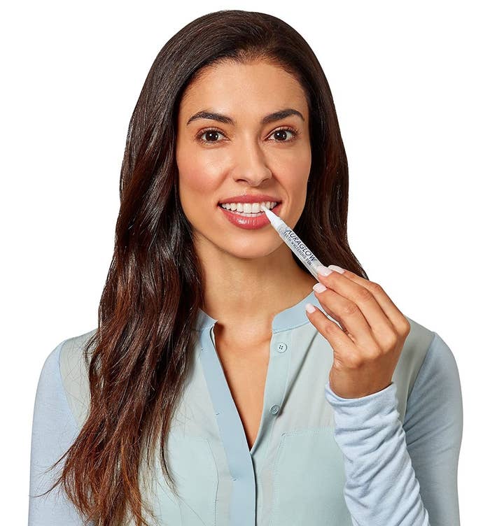 A woman holding a teeth whitening pen near her teeth