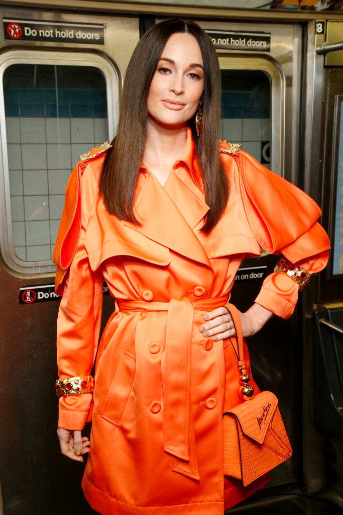 Kacey Musgraves attends the Moschino Prefall 2020 Runway Show in a brightly-colored trench coat with matching purse