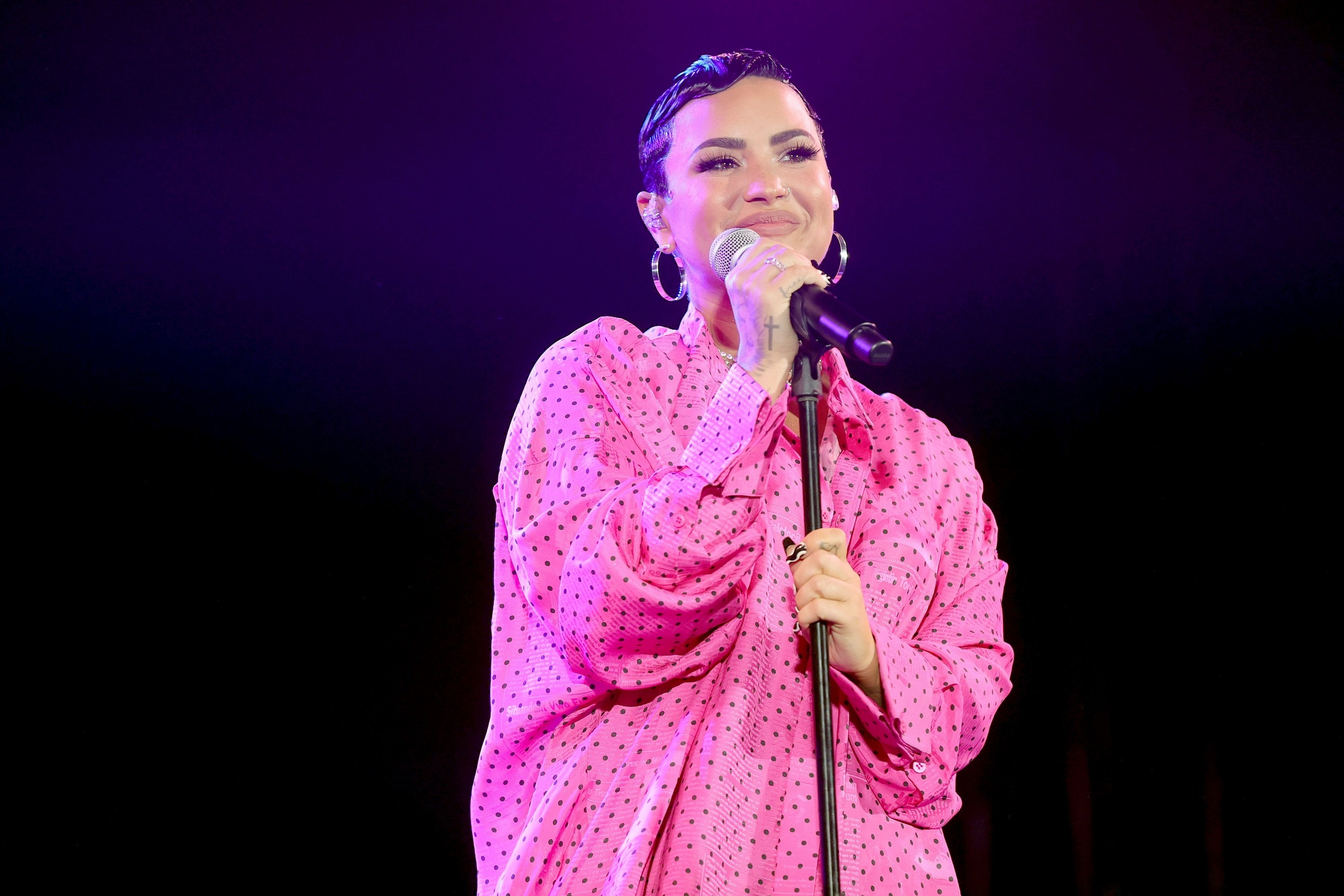 Demi performing on stage in a polka dot ensemble and rocking short hair