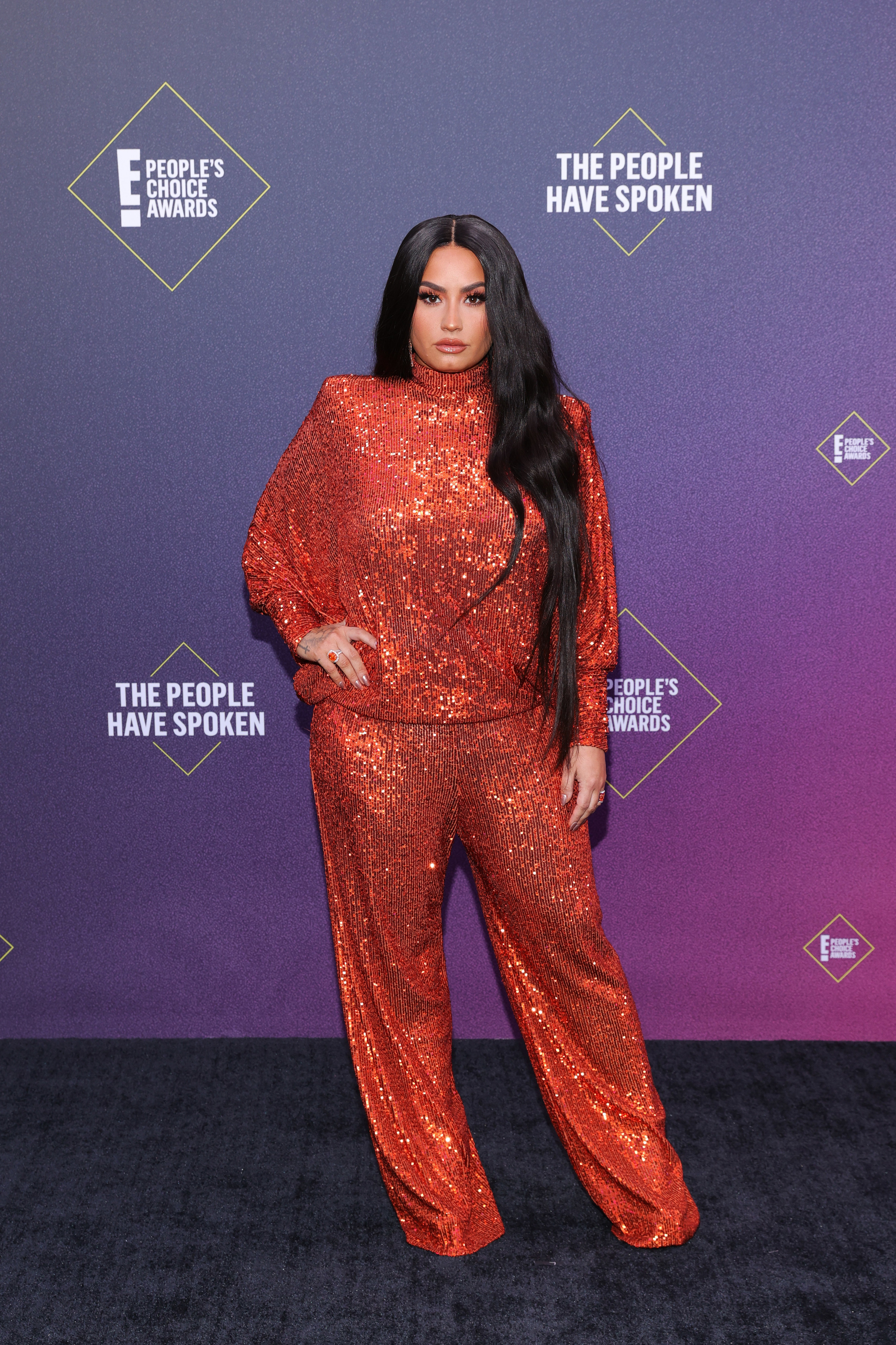Demi posing for photographers at an event in a sequined jumpsuit and rocking long hair