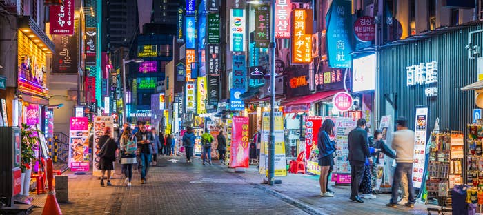 Crowds of shoppers along the pedestrianized streets of Myeong-dong overlooked by the neon lights of stores in the heart of Seoul at night