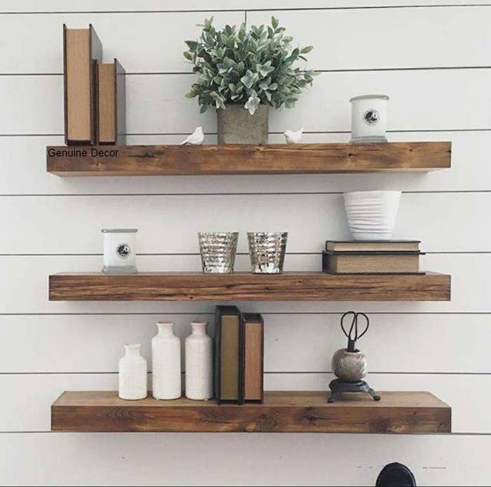 3 wooden wall mounted shelves with books, show pieces, candles and potted plants arranged