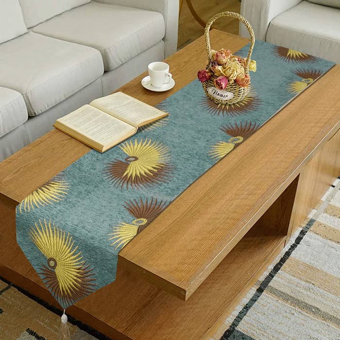 A cotton table runner in teal with yellow and ombre sun patterns embroidered on it