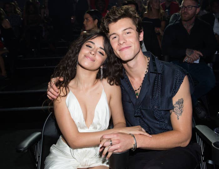 Camila and Shawn sitting down, smiling, and holding each other