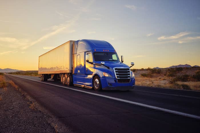 Large semi truck hauling freight on the open highway in the western USA under an evening sky.