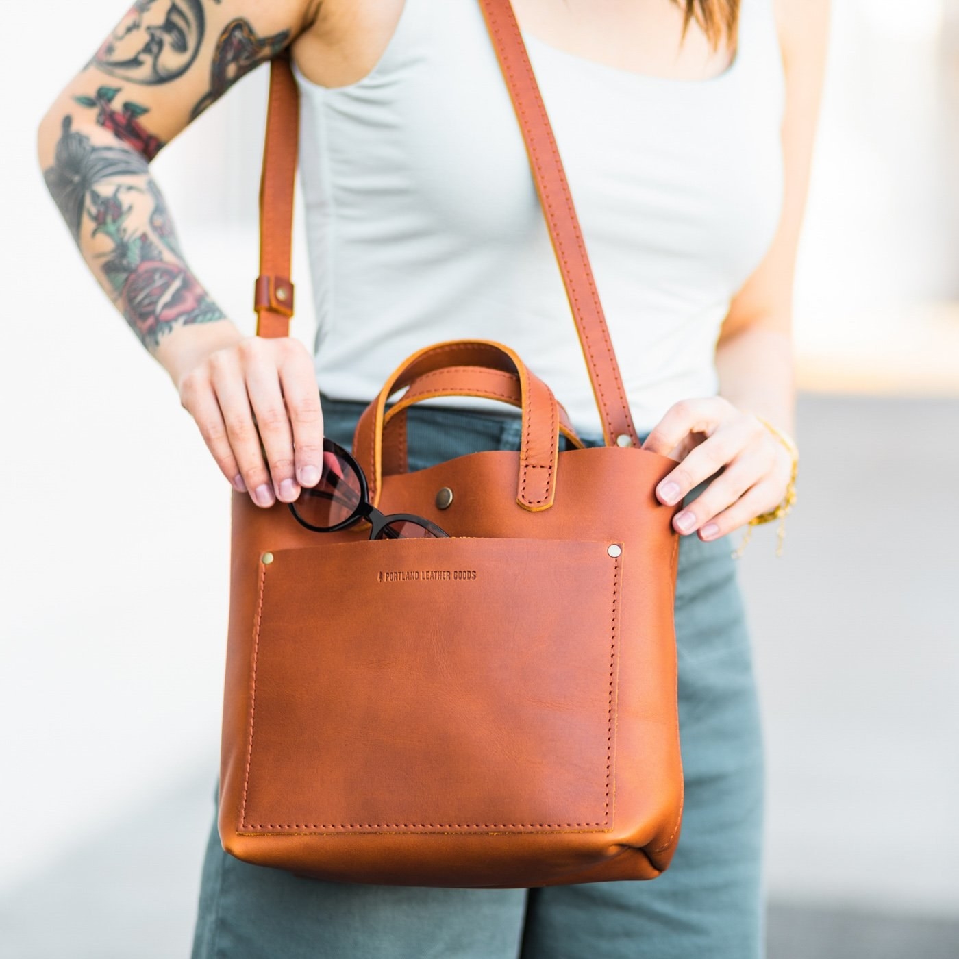 Model is taking black glasses out of a burnt orange-colored leather crossbody bag