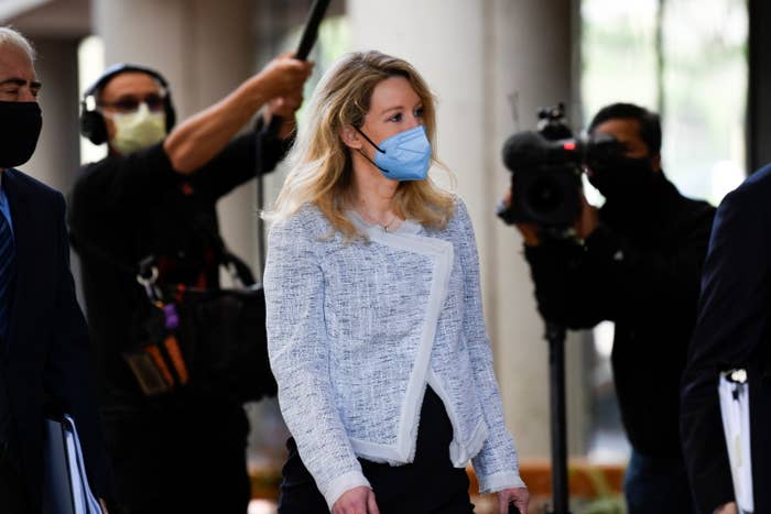 Holmes wears a face mask walks with several photographers behind her