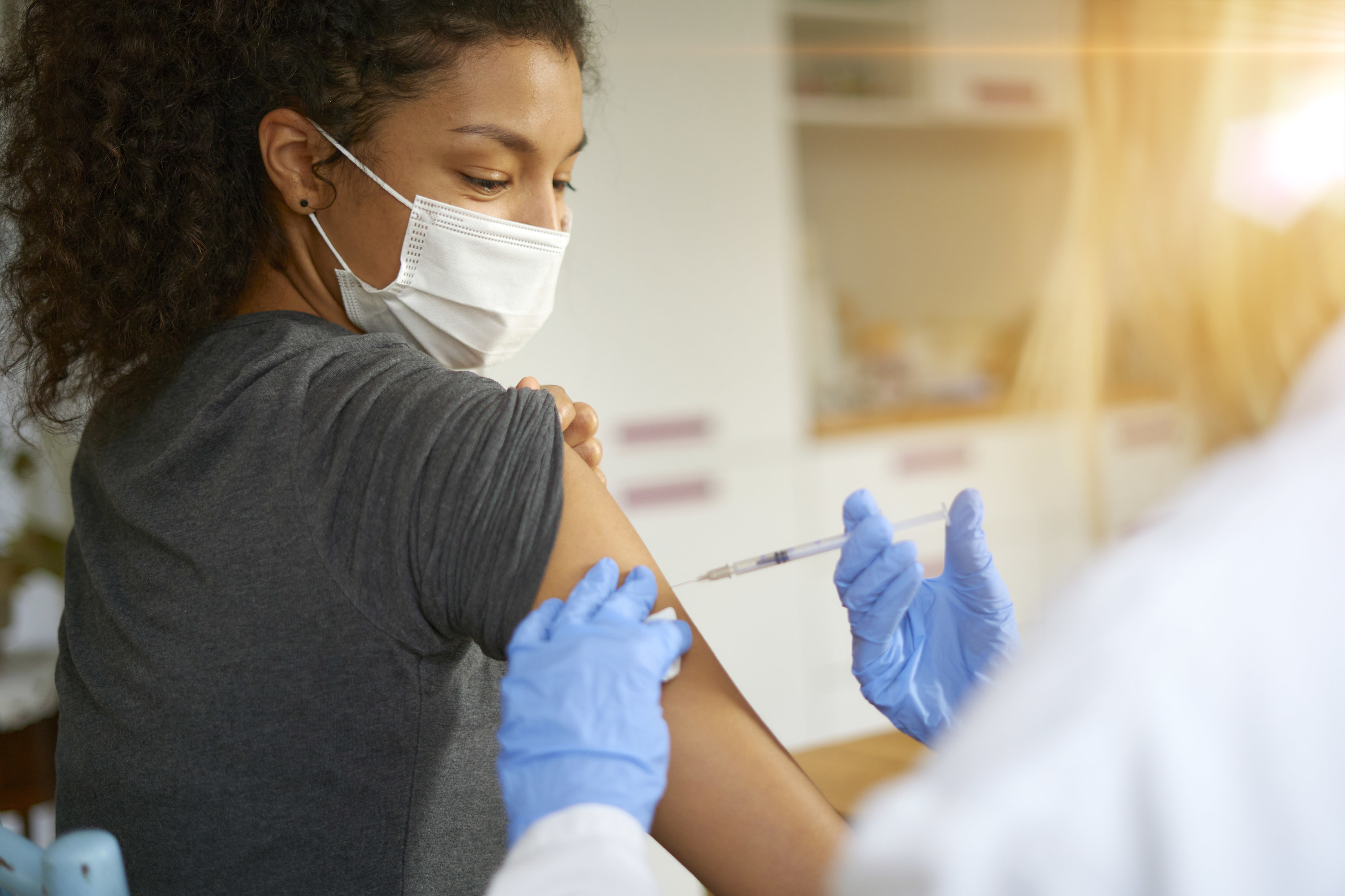An image of a woman in a face mask getting a shot in her arm of the COVID-19 vaccine