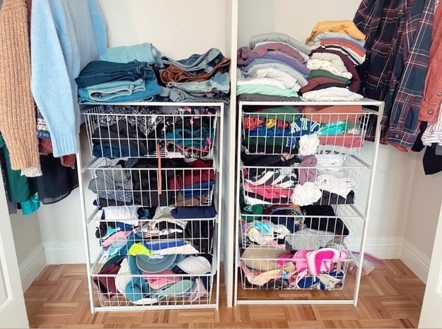 A BuzzFeed editor image of two four drawer white wire pull out standalone shelving units in a closet with clothes and accessories in them