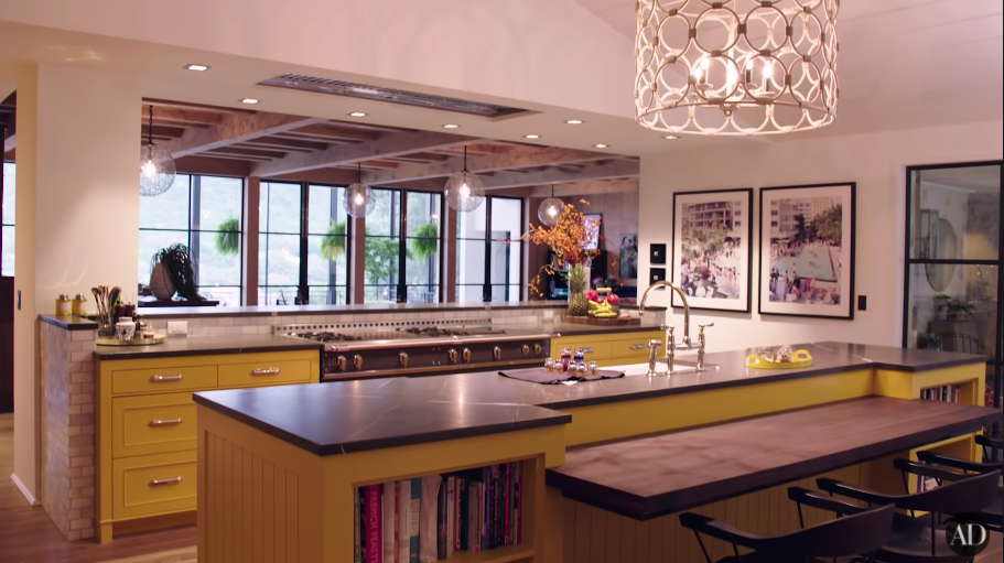 Another view of their large kitchen with paintings, large island table, and another room beyond it