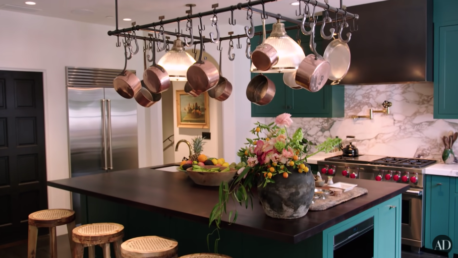 Another view of Kendall&#x27;s kitchen with pots and pans hanging above an island table with stools