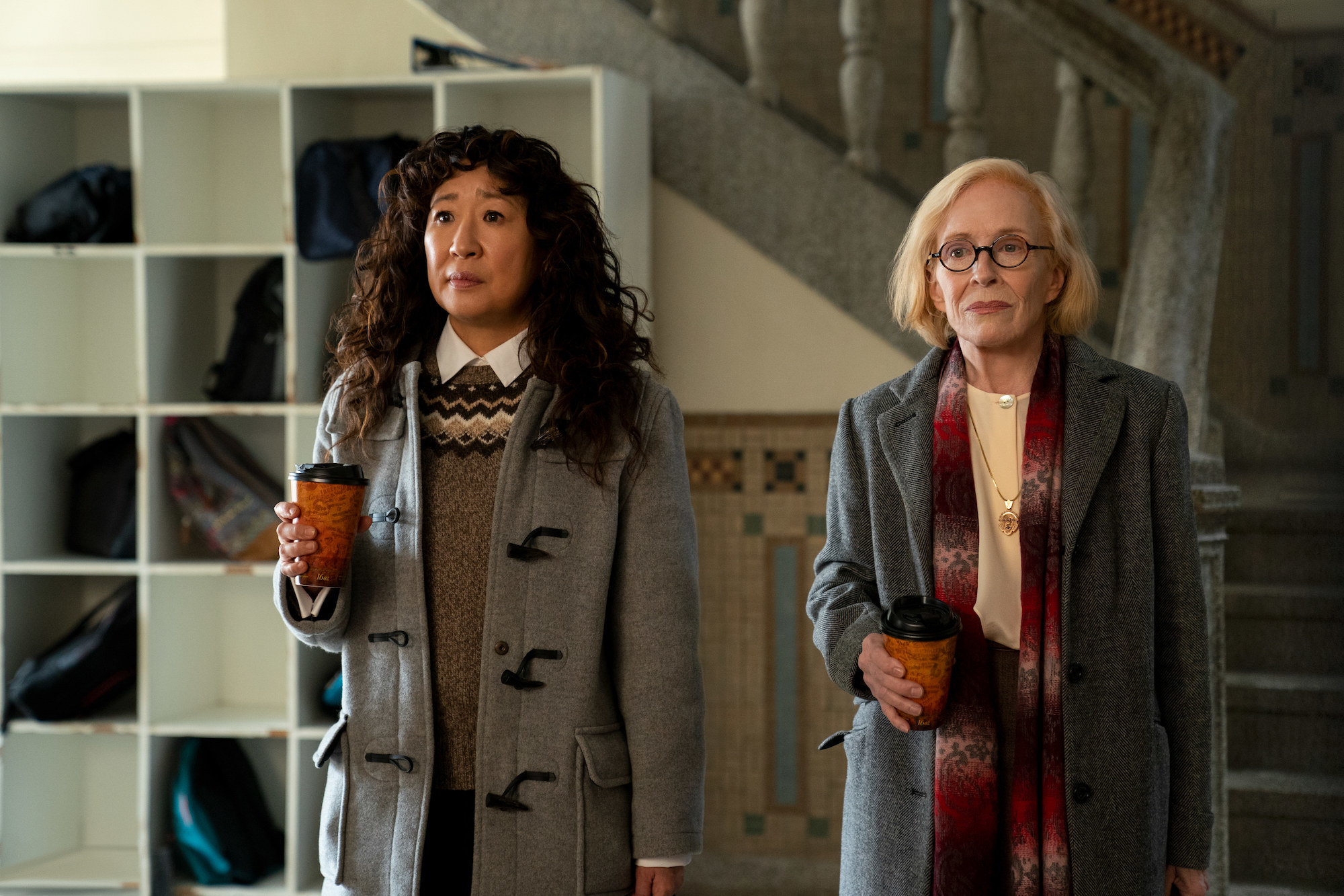 Photo of Sandra Oh and Taylor Holland in The Chair dressed in winter clothes, holding coffees